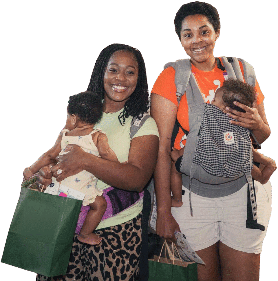 Two moms holding their babies, smiling at the camera.